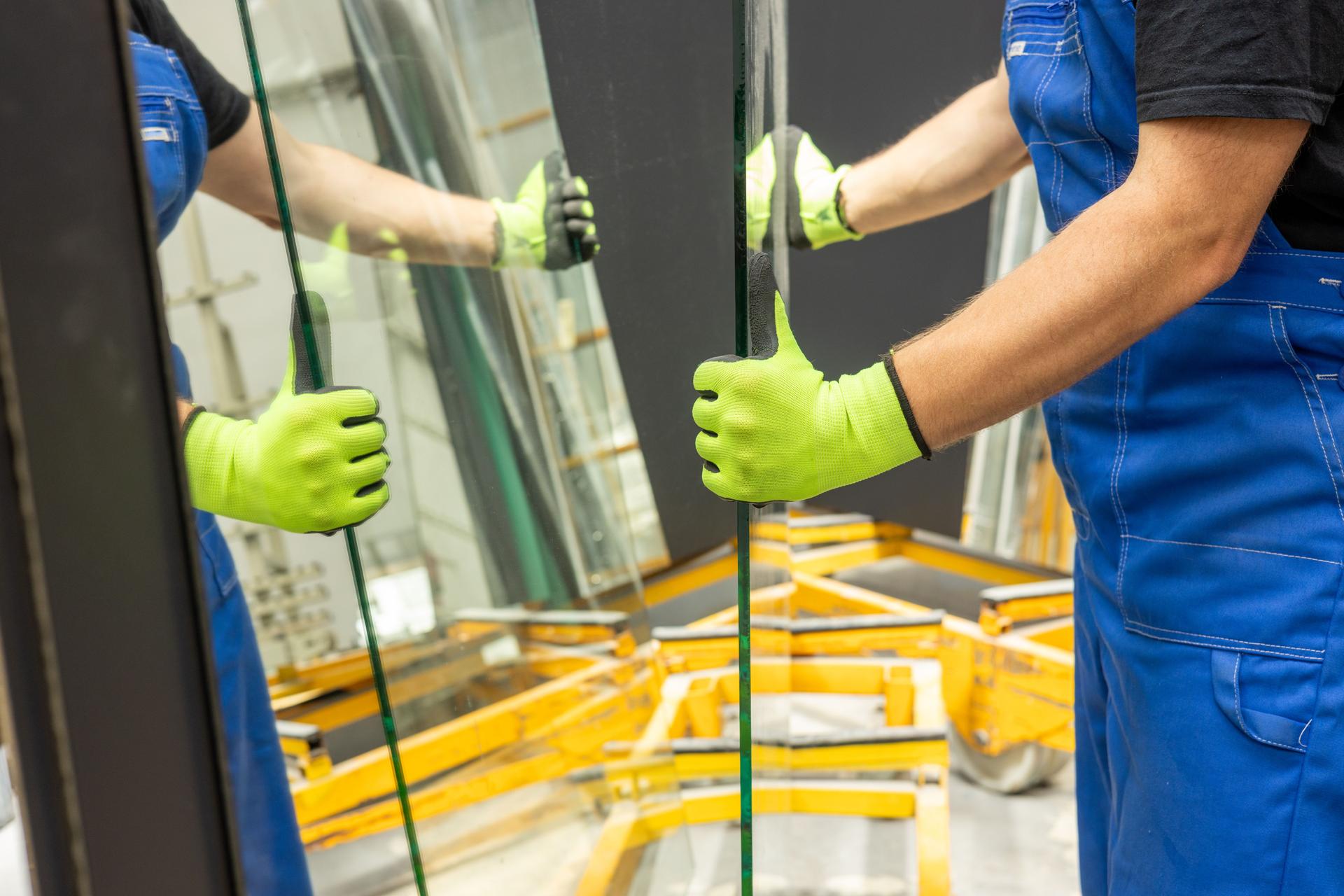 A glazier picks up sheets of thick glass from a rack in a glass factory, many mirrors cause mirror reflections, close up