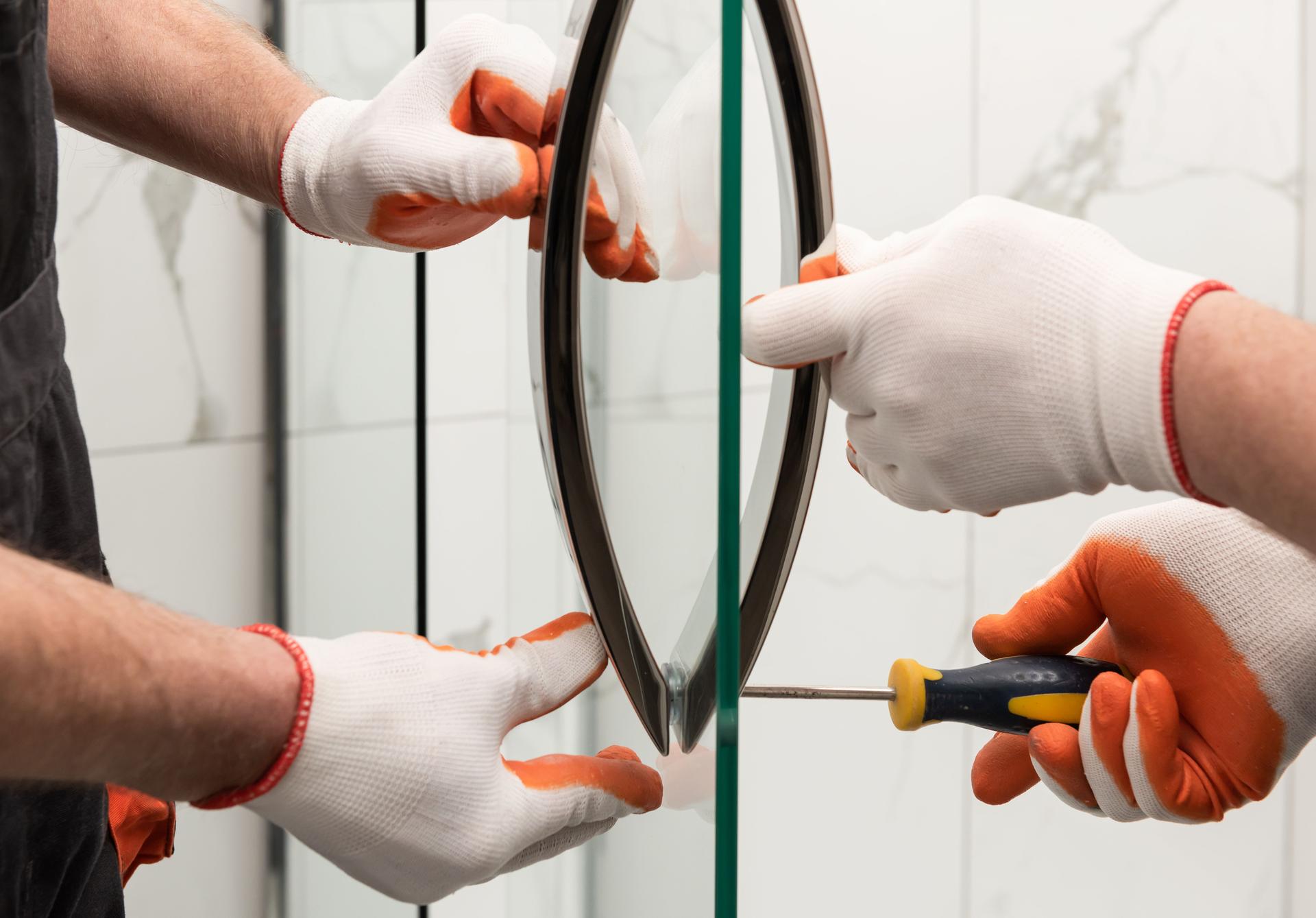 Workers are mounting door handles of the shower enclosure.