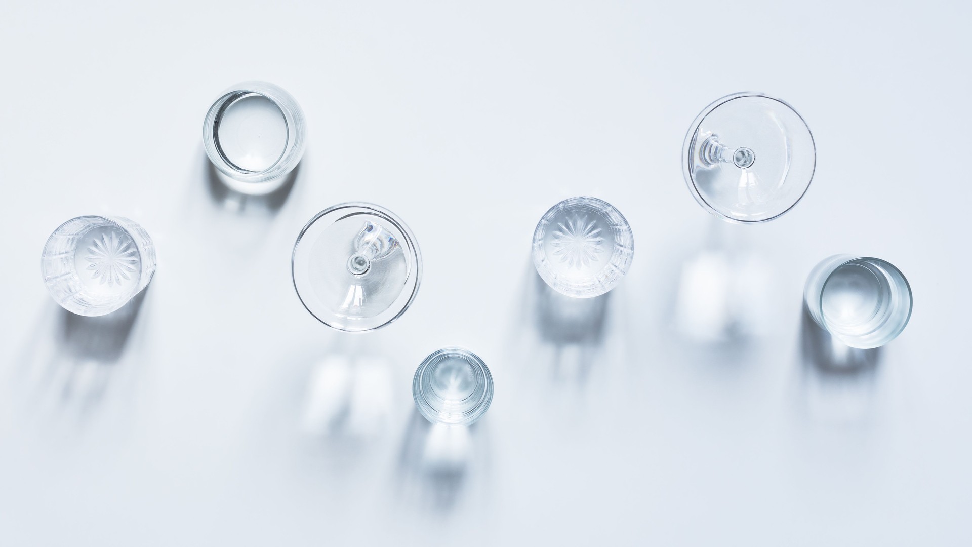 Variety of many transparent glasses with clear water on white background with shadows top view.